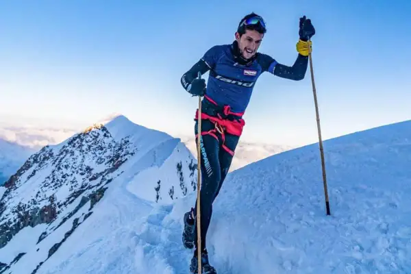 Manuel Merillas, le coureur de trail, franchit une crête enneigée, bâtons en main, sous un ciel bleu éclatant.