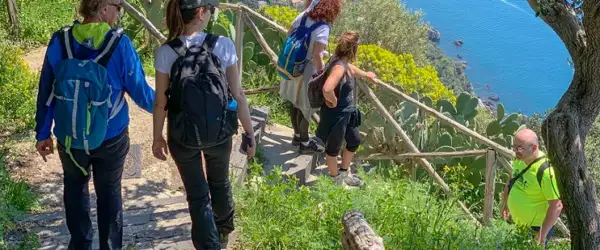 Gruppo di escursionisti sul sentiero degli dei ad Agerola, con vista sul mare blu e vegetazione mediterranea.