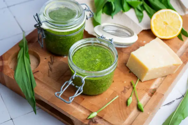 Frisches Bärlauchpesto in Gläsern, bereit für ein köstliches pesto rezept. Daneben ein Stück Parmesan, Zitrone und Bärlauch.