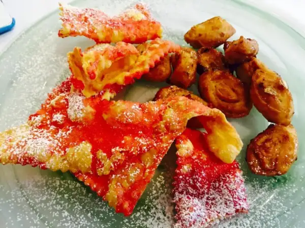 Dolci di carnevale marchigiani: chiacchiere rosse e frittelle dorate, cosparse di zucchero a velo, un piacere per gli occhi e il palato.