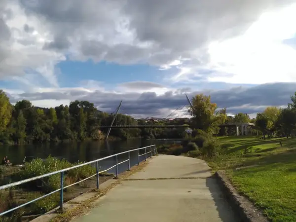 Paseo junto al río Miño, con el puente del Milenio y la playa fluvial de Ourense al fondo. Nubes amenazantes en el cielo.