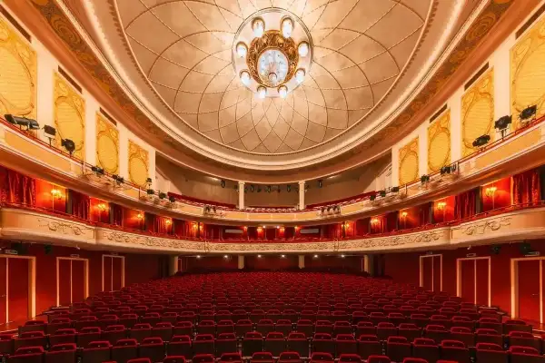 Wnętrze teatru z czerwonymi fotelami i bogato zdobionym sufitem, gotowe na wspaniały performance.