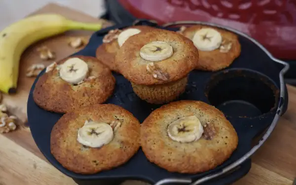 Frisch gebackene Bananen Nuss Muffins, garniert mit Bananenscheiben und Walnüssen, liegen in einer Muffinform.