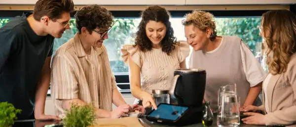 Pięć osób przygląda się ekranowi urządzenia kuchennego, szukając inspiracji na thermomix top 10 przepisów.