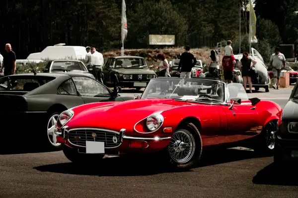 Roter Oldtimer-Cabriolet glänzt auf einem Treffen in Berlin. Im Hintergrund weitere Klassiker und Besucher.