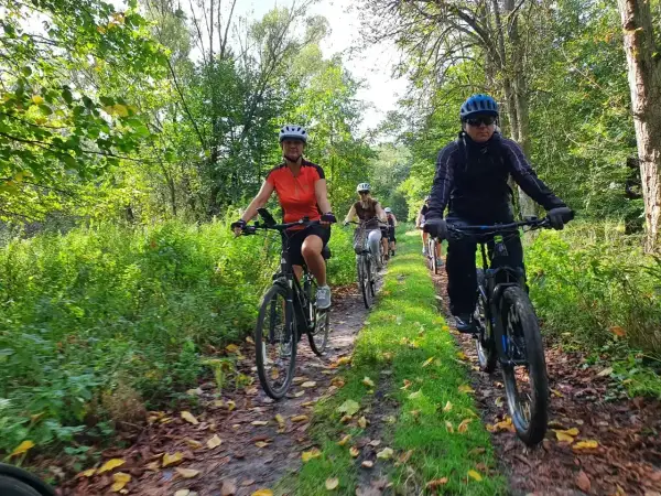 Grupa rowerzystów przemierza malownicze milickie trasy rowerowe wśród zieleni i jesiennych liści.