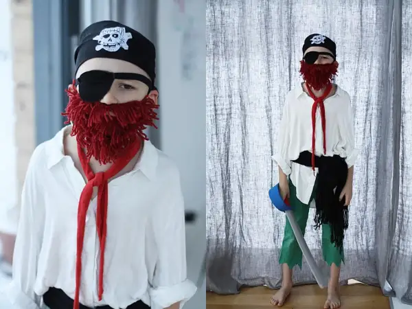 Chłopiec w stroju pirata: czarna bandama z czaszką, opaska na oko, czerwona broda z włóczki, biała koszula, zielone spodnie. Jak zrobić strój pirata dla chłopca.