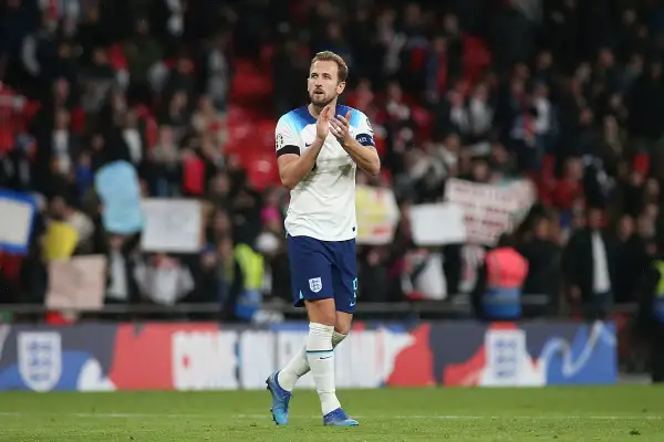 Harry Kane, w białej koszulce Anglii, klaszcze na tle trybun. Choć nie wiemy, ile lat ma Harry Kane, jego forma na boisku mówi sama za siebie.