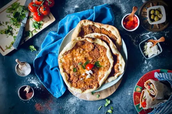 Lahmacun rezept original: Fladenbrot mit Hackfleisch, Tomaten, Petersilie und Käse, daneben Oliven und ein Wrap.