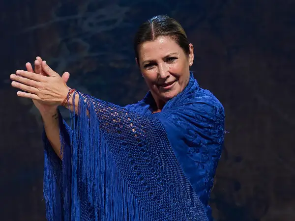 Sara Baras, joven y vibrante, luce un mantón azul eléctrico con flecos, sus manos en un gesto flamenco.