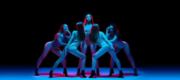 Pięć kobiet w body i butach na obcasach wykonuje zmysłowy taniec high heels w neonowym świetle.