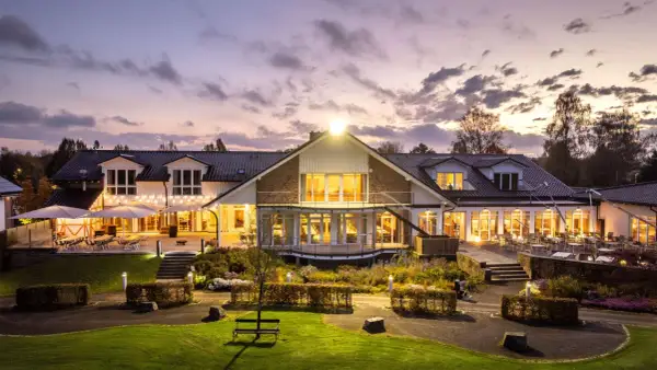 Abendstimmung am Golfclub Heckenhof. Beleuchtetes Clubhaus mit Terrassen und Gartenanlage im Dämmerlicht.
