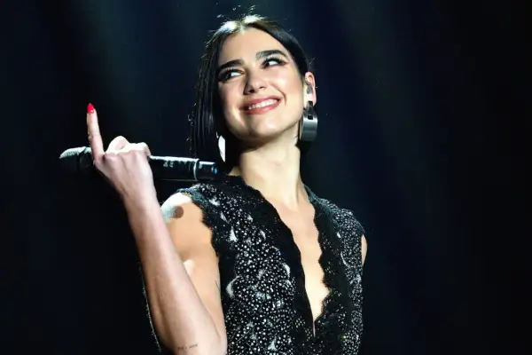 Uśmiechnięta Dua Lipa z mikrofonem w dłoni, podczas jednego ze swoich ekscytujących koncertów.