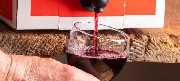 Czerwone wino leje się z kartonu do kieliszka. Wygodny sposób na serwowanie wina w 5 litrowej butelce.
