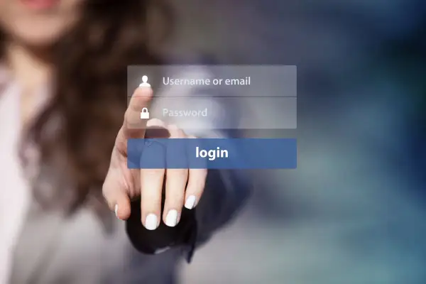 Dłoń naciska przycisk logowania. Widoczne pola na username i hasło, sugerujące proces uwierzytelniania.