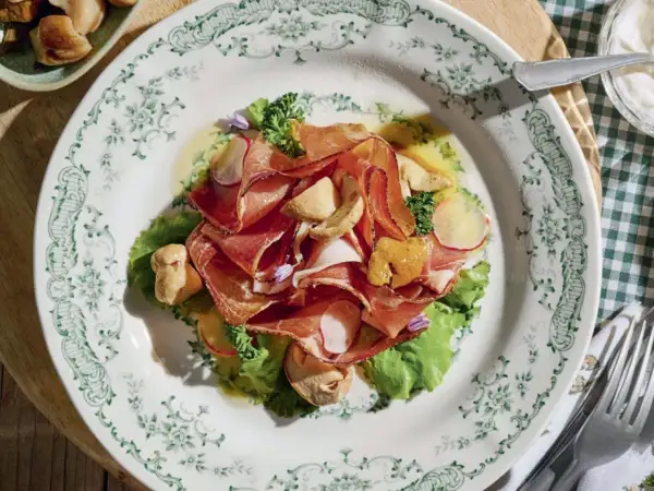 Deliziosi antipasti di terra con affettati rosa, funghi e verdure fresche su un piatto decorato.