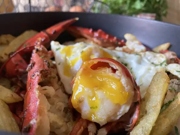 Deliciosos huevos rotos con bogavante, patatas fritas crujientes y un huevo con la yema perfecta.