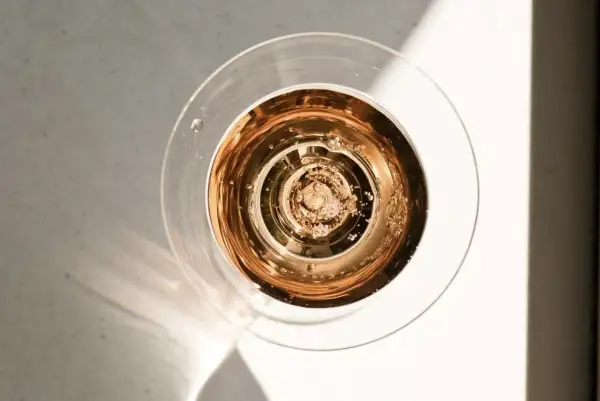 Szklanka z różowym, musującym winem dealkoholizowanym, w świetle słońca. Bąbelki unoszą się ku górze.