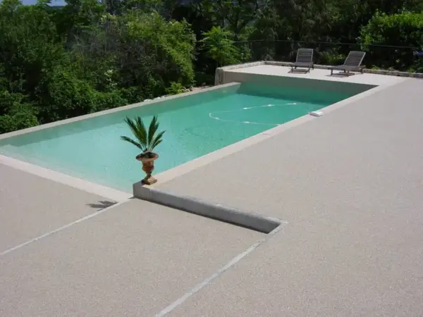 Piscina con bordo in cemento e pavimentazioni in cemento a vista, circondata da vegetazione lussureggiante.