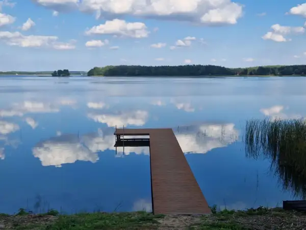 Drewniany pomost na spokojnym jeziorze przechlewskim, odbijającym błękitne niebo z białymi chmurami.