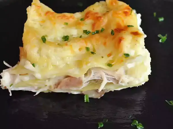 Une part de lasagnes poulet champignons, gratinée et garnie de persil frais, sur une assiette noire.