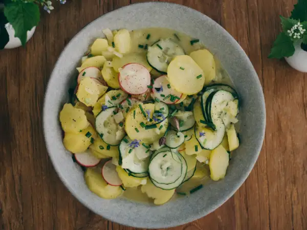 Ein Teller mit traditionellem bayrischem Kartoffelsalat, garniert mit Radieschen, Gurken und Schnittlauch.