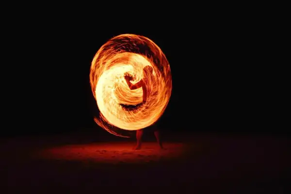 A performer creates a fiery vortex with a poi in this stunning fire photography. The flames swirl around them, illuminating the dark night.