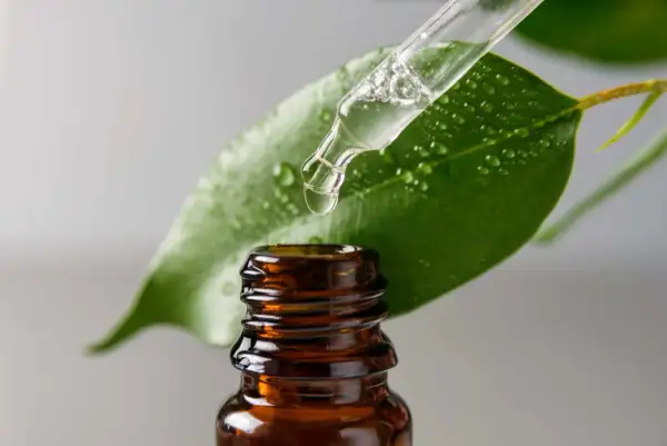 Una goccia di liquido trasparente cade da un contagocce su una foglia verde bagnata. La glicerina, cos'è? Un ingrediente idratante essenziale.