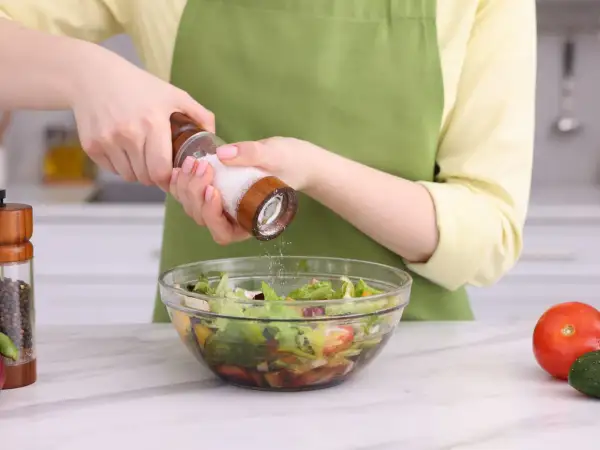 Manos sazonando una ensalada con sal, uno de los usos de la sal en la cocina.