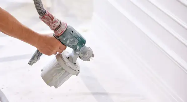 Mano che tiene un aerografo per verniciare con compressore, creando un effetto liscio su una superficie bianca.