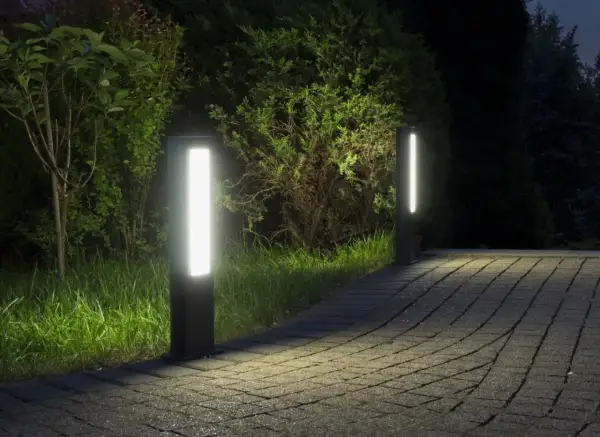 Dwa nowoczesne słupki LED oświetlają ścieżkę z kostki brukowej w ogrodzie.