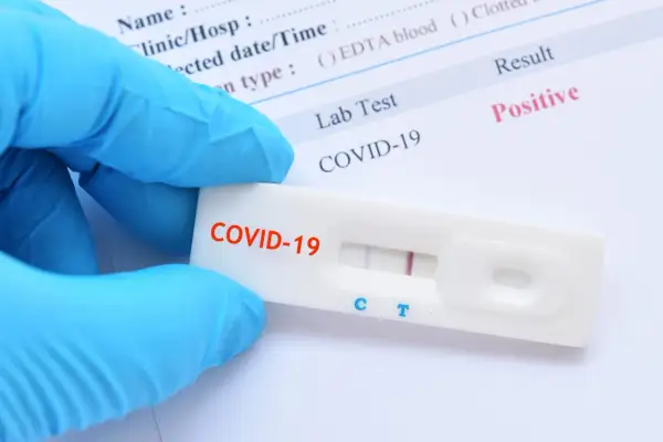 Ręka w niebieskiej rękawiczce trzyma test antygenowy COVID-19 z dwoma widocznymi liniami, co oznacza pozytywny wynik.