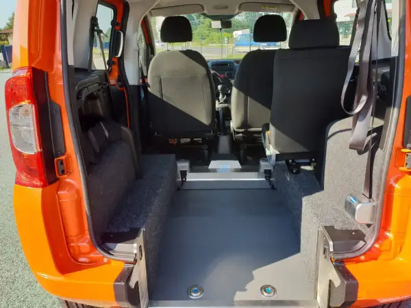 Interno di un Fiat Qubo arancione, con sedili posteriori e ampio spazio per il bagagliaio. Le dimensioni del bagagliaio sono ideali per trasporti.