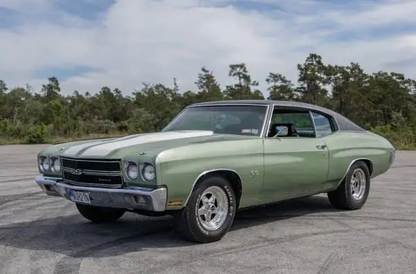 Grön Chevelle SS från 1970 med vita ränder på huven, parkerad utomhus med träd i bakgrunden.