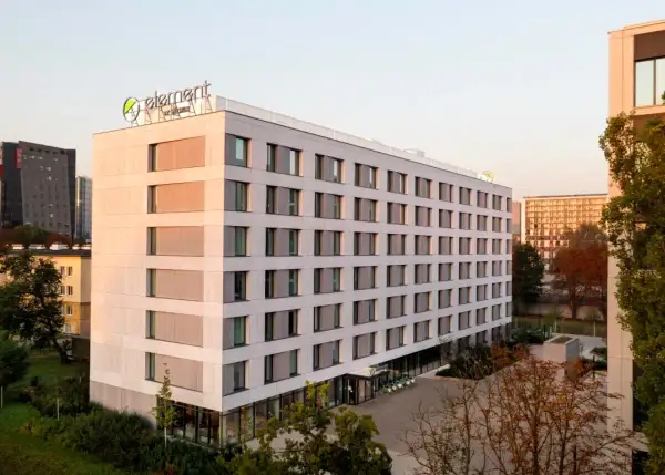 Nowoczesny hotel Element by Westin z zielonym logo na dachu, otoczony drzewami i innymi budynkami.