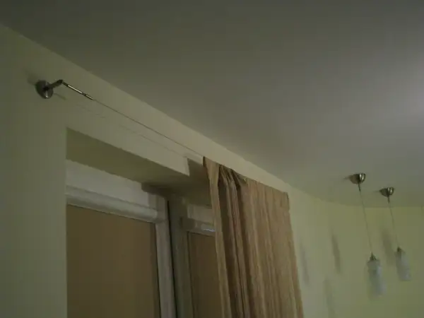 Elegancka zasłona w beżowym kolorze wisi na cienkiej lince zamiast karnisza, tworząc minimalistyczny wygląd.