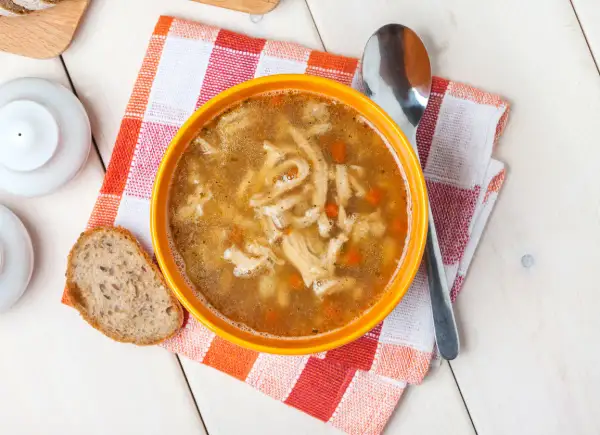 Aromaticzne flaki po zamojsku w pomarańczowej misce, obok kromka chleba i łyżka.