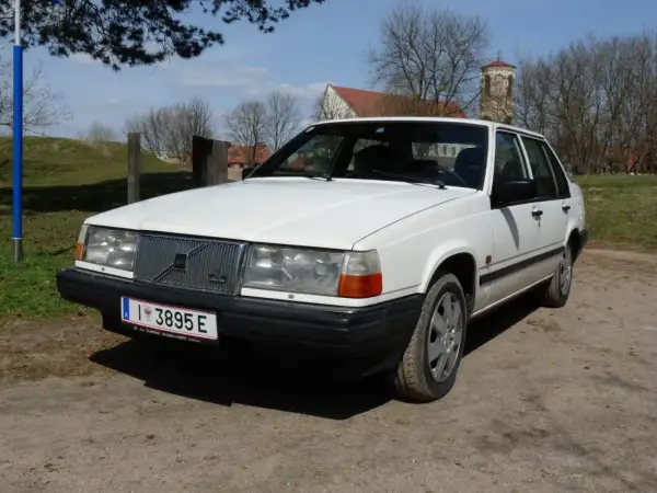 Białe Volvo 840 z przodu, na tle drzew i kościoła.