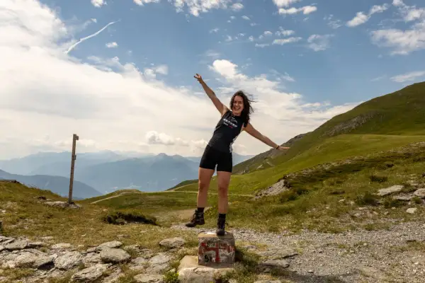 Glückliche Frau mit ausgestreckten Armen auf einem Berg in den Alpen, ein Zeichen für ihr Backpacking Europa Abenteuer.
