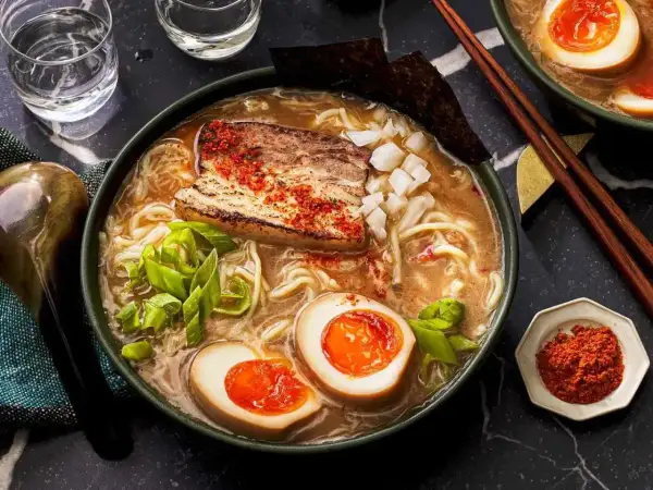 A miska pełna aromatycznego ramen co to jest? Makaron, jajko na pół, kawałek mięsa i szczypiorek w bulionie.
