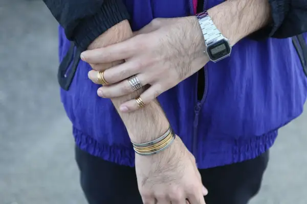 Combinaciones de pulseras y anillos dorados y plateados en brazos y muñecas, con reloj digital.