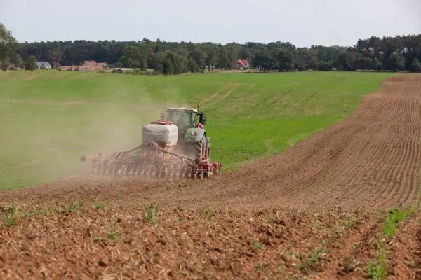 Traktor sieje, dodając do gleby niezbędne fosforany. W tle zielone pola i las.