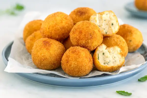 Un piatto di polpette di ricotta dorate e croccanti, alcune intere, altre spezzate per mostrare il ripieno morbido e profumato.