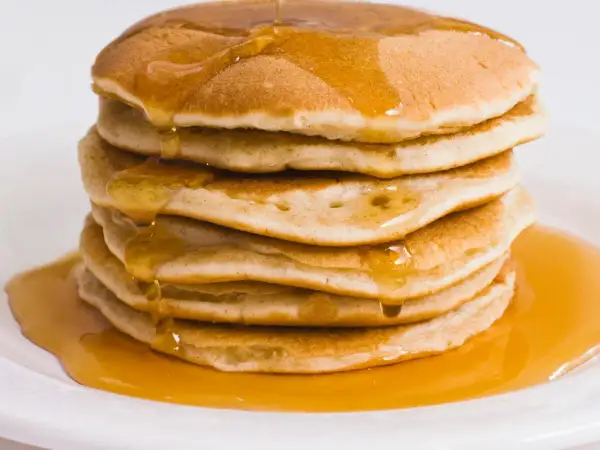 Pila di pancake proteici dorati, inzuppati di sciroppo d'acero che cola.