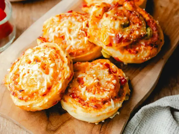 Leckere Pizzaschnecken aus Pizzateig, überbacken mit Käse und Tomaten, liegen auf einem Holzbrett.