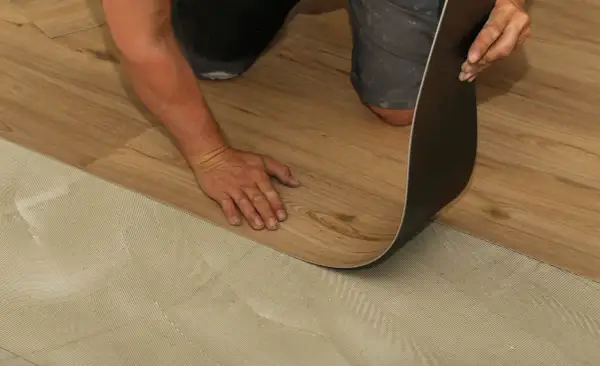 Hand verlegt Laminat auf PVC-Boden. Der Kleber ist auf dem Untergrund aufgetragen, bereit für das neue Bodenmuster.