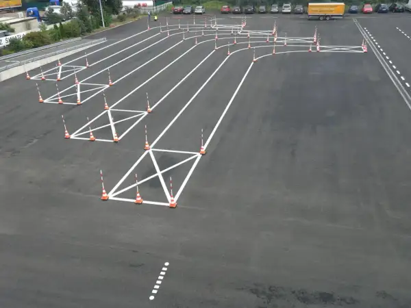 Plac manewrowy z pachołkami i białymi liniami, idealny do nauki, jak kręcić kierownicą podczas jazdy po łuku.