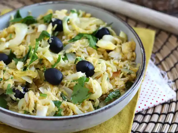 Un plat de bacalhau à bras, mélange savoureux de morue effilochée, d'oignons, d'œufs brouillés et d'olives noires, garni de persil frais.