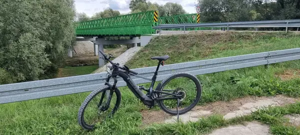 Rower elektryczny czeka na przygodę na trasie w Kazimierzu Dolnym. Zielony most w tle zaprasza do odkrywania malowniczych zakątków.