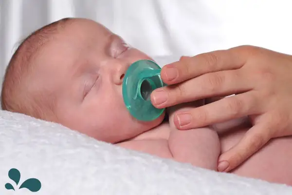 A hand gently offers a pacifier to a sleeping baby. Learn when to introduce a pacifier to a breastfed baby for optimal comfort.